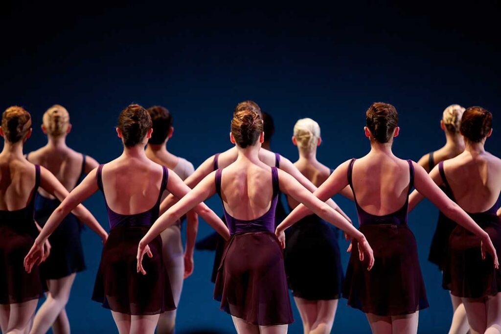 Three adults participating in a lively group dance class in a bright, spacious studio.