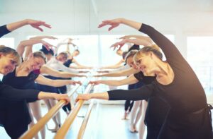 Dancers warm up with controlled leg swings and gentle stretches on a studio floor.