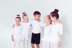 Parent watching a young dancer practice footwork in a bright studio with dance shoes nearby